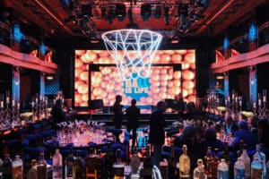 Event design featuring a vibrant basketball-themed setup with a large illuminated hoop and "Ball Is Life" display, surrounded by elegantly arranged tables and guests, showcasing Geo Events' expertise in corporate event production.
