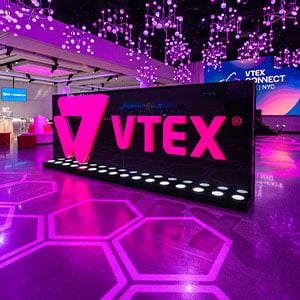 VTEX branding display with vibrant pink lighting, hexagonal floor design, and modern event setup, showcasing corporate event production by Geo Events.