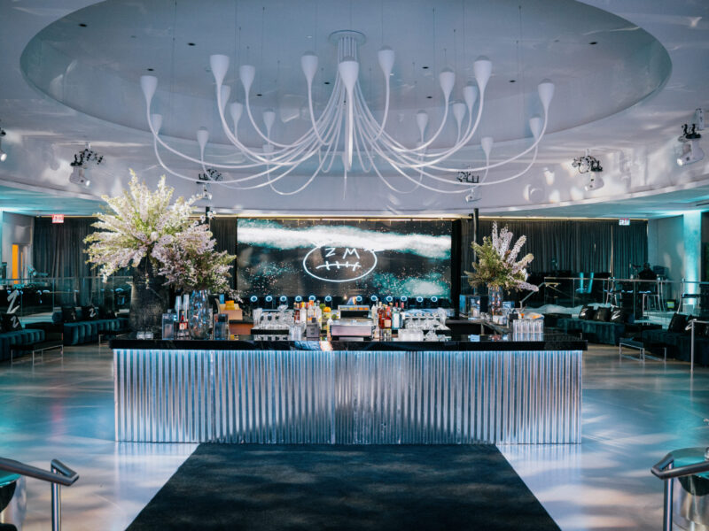 Corrugated galvanized metal-clad bar with black top, LED wall with graffiti smiley logo, white branches and navy lounge